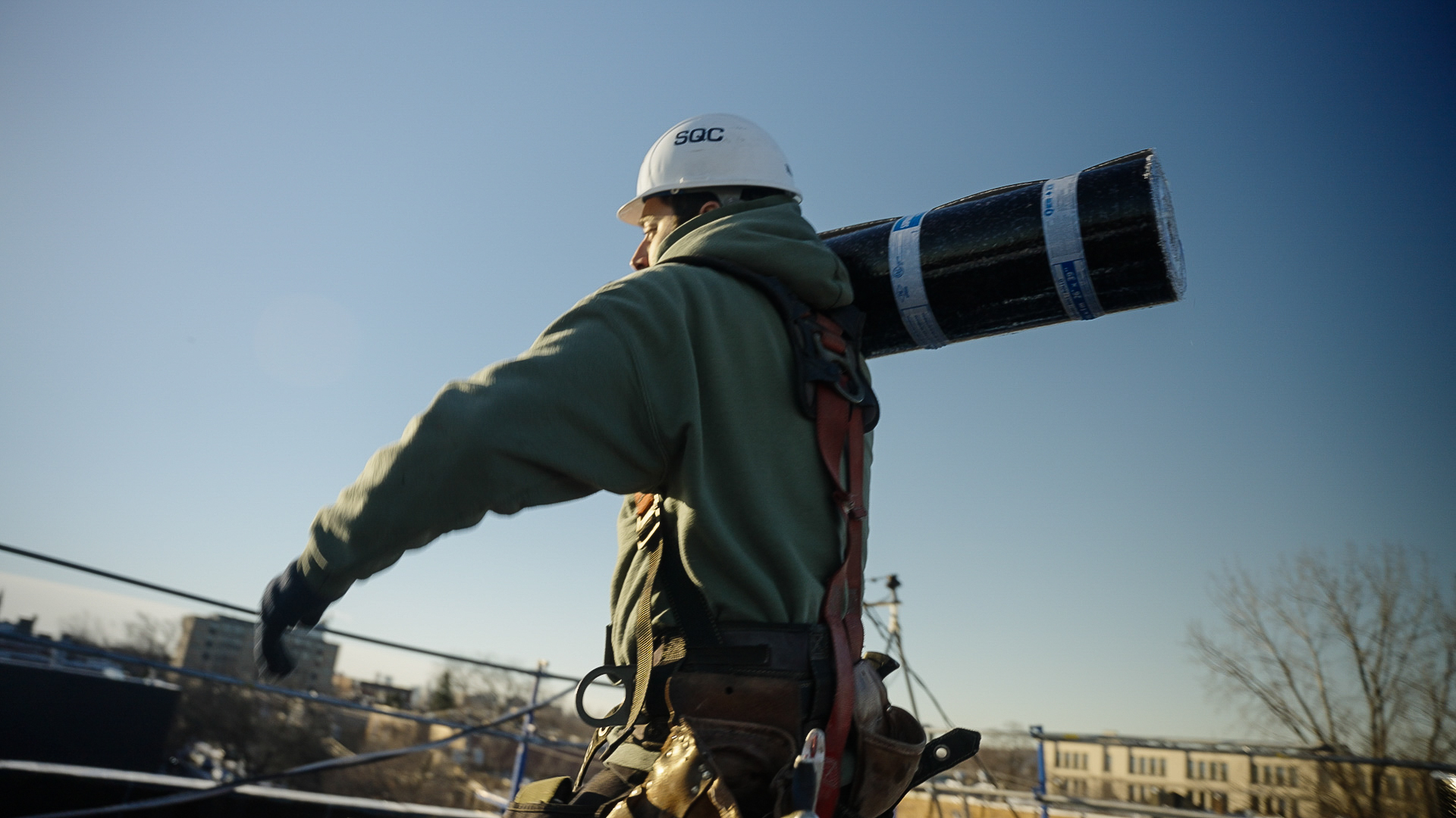 Couvreur Toitex transportant un rouleau de membrane sur son épaule
